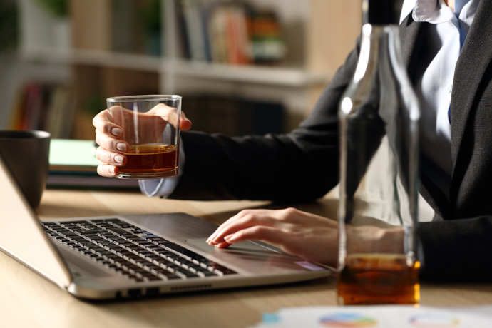 mujer bebiendo alcohol delante de portatil