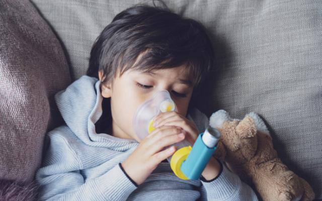 Niño con inhalador que sufre de asma infantil.