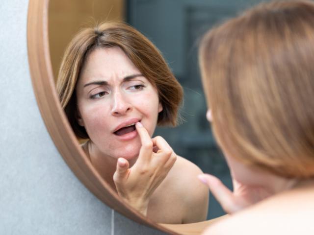 Mujer examinando en el espejo sus manchas marrones en los dientes. 