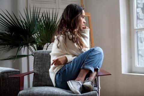 Chica sentada mirando por la ventana que quiere saber cómo calmar la ansiedad.